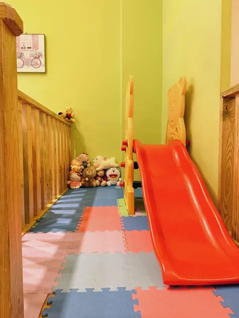 美夢成真的兒童遊戲區，紅色溜滑梯、鋪滿地墊的地板與一整排絨毛玩偶